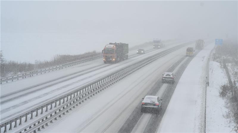 Autos und Lkw sind auf einer Autobahn unterwegs. Der Schnee ist ein Hindernis. Die Lkw müssen häufig trotzdem fahren.