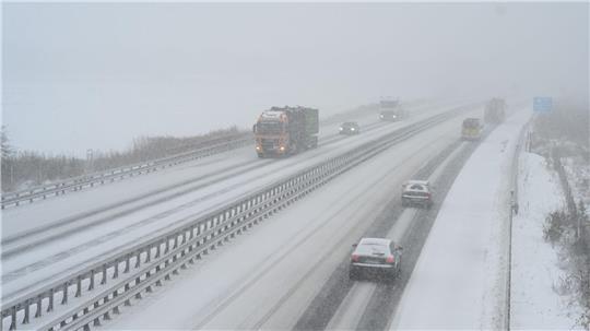 Autos und Lkw sind auf einer Autobahn unterwegs. Der Schnee ist ein Hindernis. Die Lkw müssen häufig trotzdem fahren.