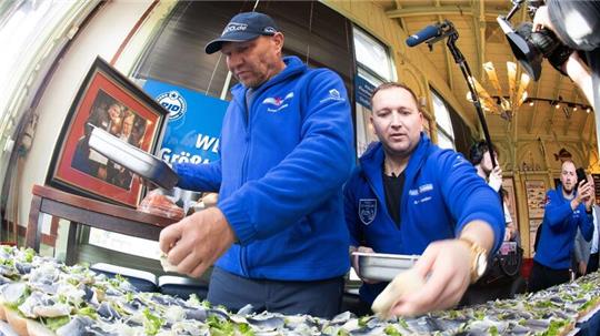 Axel Schulz, ehemalige Profiboxer (l-r), und André Domke, Fischsommelier und -händler, belegen das gigantische Fischbrötchen mit Salat, Fisch und Zwiebeln.