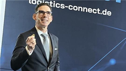BLG-Chef Matthias Magnor hält auf der Messe Logistics-Connect eine 50-Cent-Münze hoch, um zu verdeutlichen, wie wenig Geld der Bund jährlich den deutschen Häfen zur Verfügung stellt. 