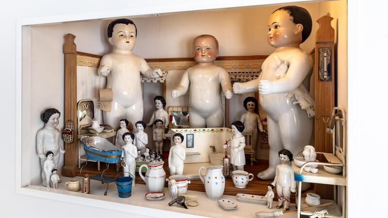 Von Porzellanpuppe bis Barbie: Auf Zeitreise im Puppenmuseum Falkenstein Mehre Puppen aus Porzellan in verschiedenen großen stehen in einer Vitrine.