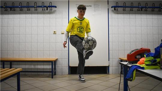Jupp Hesse im gelben Brasilien-Trikot von Ronaldinho sitzt auf einer Bank in der Kabine des TSV Großenwörden und zeigt auf die Trikotnummer 10.