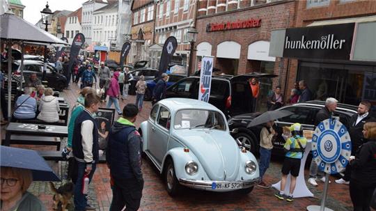 Bei der Autoschau „Buxtehude brummt“ dürfen ausnahmsweise Oldtimer durch die Fußgängerzone fahren. Hier fährt ein VW Käfer an den neuesten Modellen von Volkswagen vorbei.