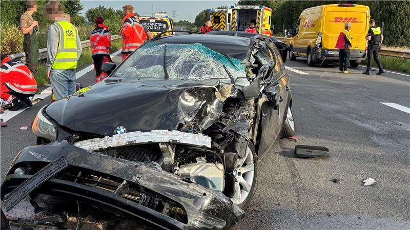 Frontalansicht eines verunglückten BMWs auf der Autobahn A26 am Morgen des 12.8.2025, dahinter sind Fahrzeuge des Rettungsdienstes sowie ein zweites am Unfall beteiligtes Fahrzeug zu sehen.  