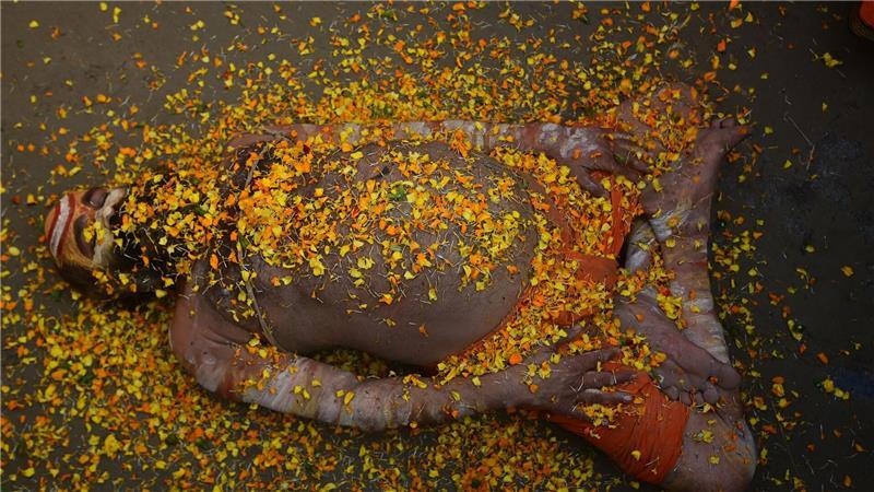 Bei einem hinduistischen Frühlingsfest in Indien liegt ein Sadhu mit Blütenblättern bedeckt auf der Straße. 