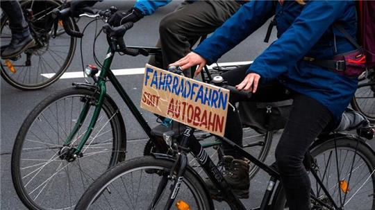 Bei einer Demo fährt ein Fahrradfahrer mit einem Schild mit der Aufschrift „„Fahrradfahr’n“ statt Autobahn“.