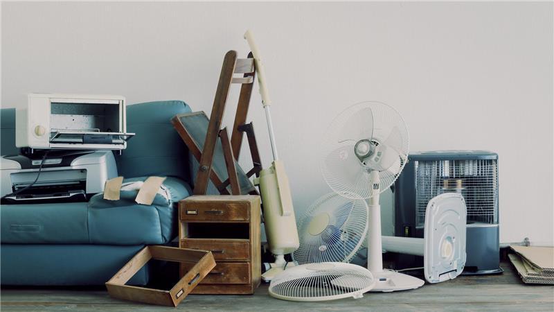 Schränke, eine Mikrowelle, eine Couch, Ventilatoren und andere alte Gegenstände stehen auf dem Boden.