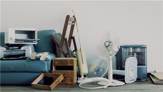 Schränke, eine Mikrowelle, eine Couch, Ventilatoren und andere alte Gegenstände stehen auf dem Boden.