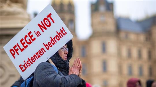 Bei einer Protestaktion vor dem Schweriner Landtag hält eine Teilnehmerin ein Schild mit der Aufschrift „Pflege in Not - Existenzen bedroht!“.