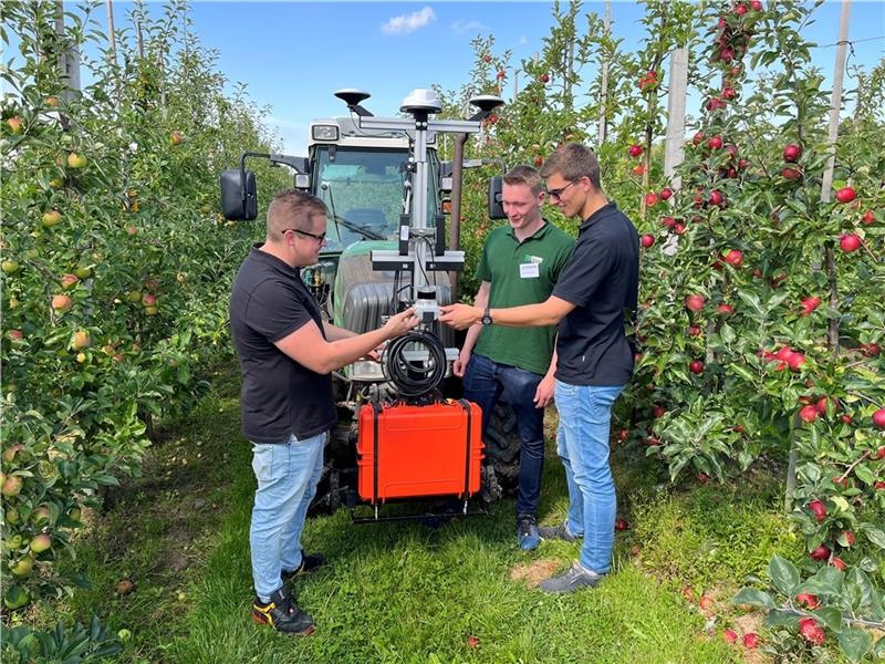 Benjamin Schulze (links) und David Berschauer (rechts) vom Fraunhofer Institut im Gespräch mit Moritz Hentzschel vom Obstbauzentrum Esteburg. Vor dem Schlepper ist die Sensorbox montiert. Foto: Vasel