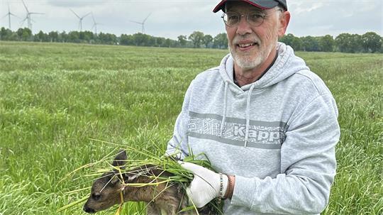 Bernd Schroetter hebt ein Rehkitz aus dem Gras - und bewahrt es so davor, auf der Wiese bei Mäharbeiten getötet zu werden.