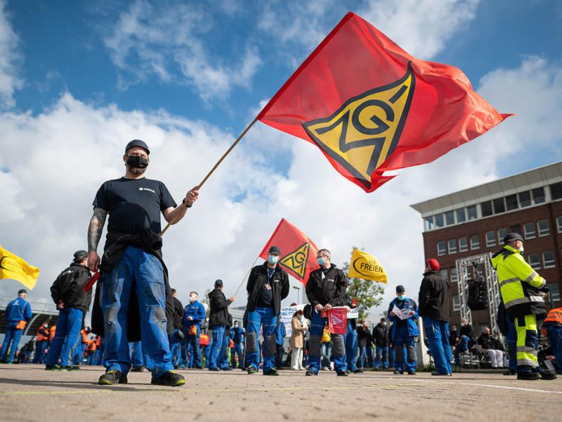 Beschäftigte des Airbus-Werkes in Finkenwerder stehen während einer außerordentlichen Betriebsversammlung vor den Toren des Werksgeländes und schwenken Fahnen der Gewerkschaft IG Metall Archivfoto: Daniel Reinhardt/dpa