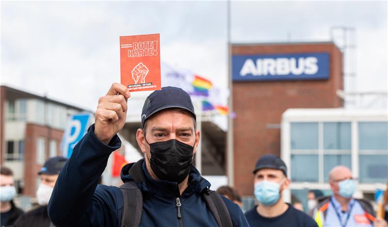 Beschäftigte des Airbus-Werkes in Finkenwerder stehen im Mai während einer außerordentlichen Betriebsversammlung vor den Toren des Werksgeländes und zeigen dem Management des Unternehmens dabei symbolisch die rote Karte. Foto: Daniel Reinhardt/dpa