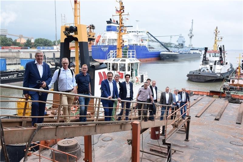 Besuch im Stader Seehafen : Vorn die Gruppe der CDU-Landtagsabgeordneten mit Vertretern der Hafenwirtschaft, hinten löscht die „Bulkness“ an der Nordwest-Pier 28 000 Tonnen Mineralgemisch für den Straßenbau oder für Wege zu Windkraftanlagen
