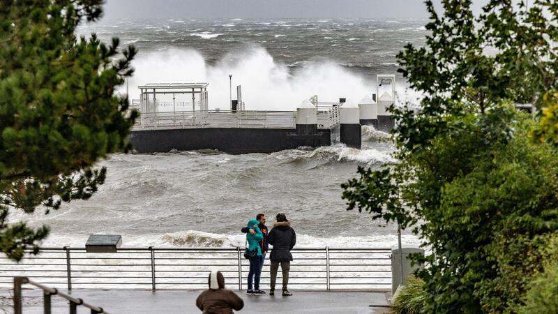 Besucher des Hafens in Schilksee fotografieren die über die Hafenanlagen niedergehenden Wellen.