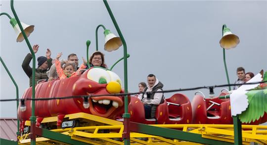 Besucher fahren mit der Erdbeer-Raupenbahn im Außenbereich von Karls Erlebnis-Dorf.