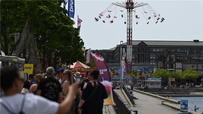Kieler Woche eröffnet: Sonne satt, wenig Wind Besucher gehen über die Kieler Woche, im Hintergrund dreht sich ein Kettenkarussell.
