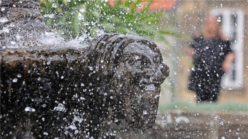 Besucher genießen bei sommerlichen Temperaturen Abkühlung an einem Brunnen im Barockgarten am Kleinen Schloss in Blankenburg.