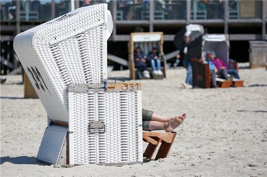 Besucher sitzen bei Sonnenschein und Temperaturen um 14 Grad Celsius in Strandkörben am Strand von St. Peter-Ording. Die Touristikerinnen und Touristiker in Schleswig-Holstein sind mit der Buchungsnachfrage zu den Pfingstferien grundsätzlich zufrieden. Foto: Bodo Marks/Bodo Marks/dpa