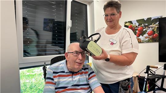 Betreuungskraft Ines Bunk hilft Hans-Uwe Bösch beim Aufsetzen der VR-Brille.
