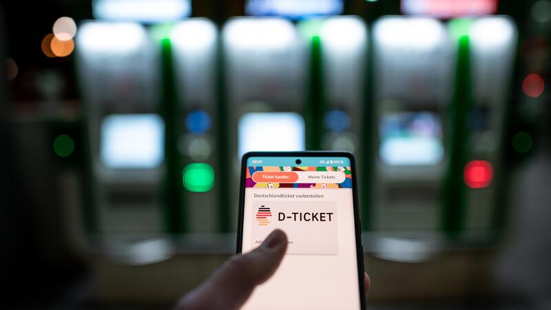 Mindestlohn, Bürgergeld, Cannabis: Drastische Änderungen in 2024 Ein Mann hält ein Mobiltelefon, auf dem das "D-Ticket" gekauft werden kann, vor Ticketautomaten am Hauptbahnhof in der Hand.