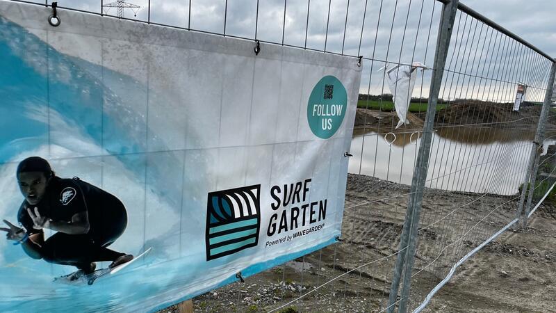 Still ruht der Surfpark in Stade: Das lange Warten auf das Verwaltungsgericht Poster vom Stader Surfgarten am Bauzaun um das Gelände des zukünftigen Surfparks.