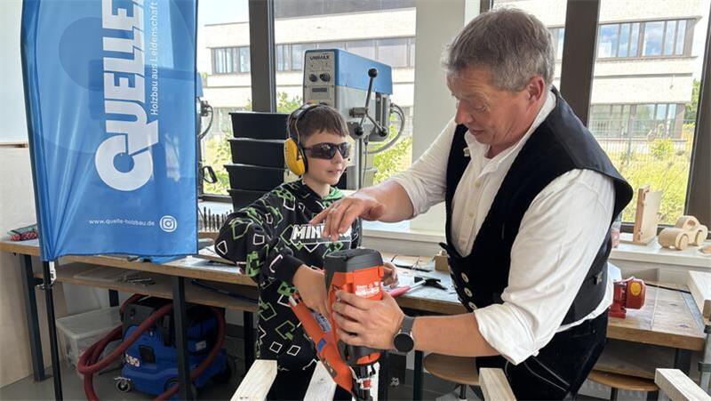 Leuchtturmprojekt: Wo Schüler mit Maurerkelle und Druckluftnagler arbeiten Björn Quelle, Geschäftsführer von Quelle Holzbau aus Bargstedt, zeigt Elias den Umgang mit dem Druckluftnagler.