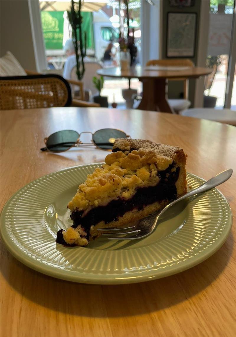 Hollywoodreif: Mit ChatGPT auf Entdeckungsreise durch Buxtehude Ein Blaubeerkuchen auf einem Teller auf einem Tisch im Cafe Pfeffertörtchen.