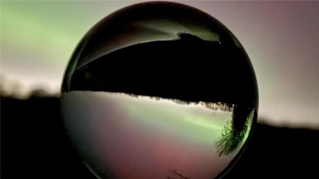 Blick auf Polarlichter durch eine Glaskugel.