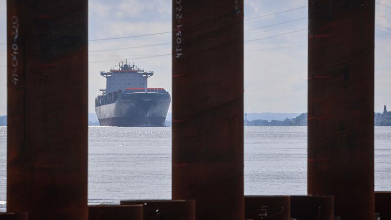 Das Containerschiff MSC Maureen fährt hinter einer Spundwand auf der Baustelle des LNG-Terminals an der Elbe in Stade. 