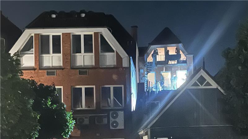 Blick aus der Straße Hasenmoor auf die Balkonseite der durchsuchten Wohnungen: Mehrere an der Razzia beteiligten Personen sind in den beleuchteten Zimmern zu sehen.