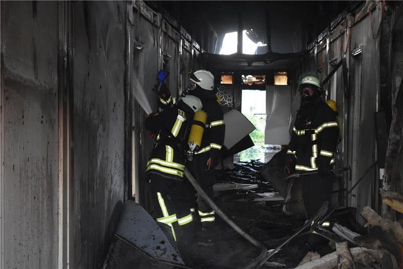 Blick in den Flur der durch Rauch und Flammen zerstörten Flüchtlingsunterkunft, Feuerwehrleute bekämpfen die letzten Brandnester. Foto: Vasel