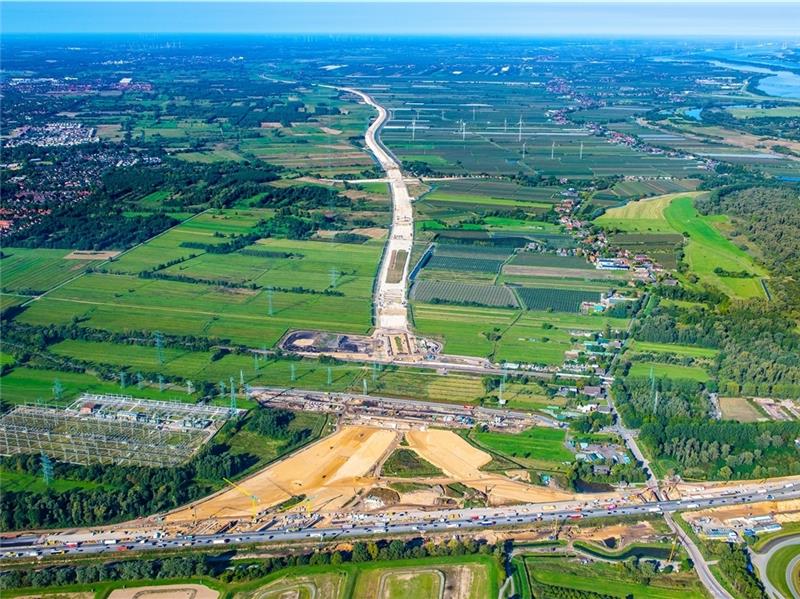 Blick vom Hamburger Hafen nach Nordwesten. Vorne verläuft die A 7, an die die A 26 angebunden wird. Gut sichtbar ist der Sanddamm in Richtung Landkreis Stade, auf dem später als letzte Schicht die Asphaltdecke aufgebracht wird. Rechts oben 