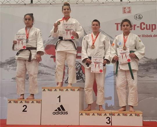 Nicole Schlej steht auf dem Podesplatz drei, trägt einen weißen Judoanzug und zeigt eine Urkunde.