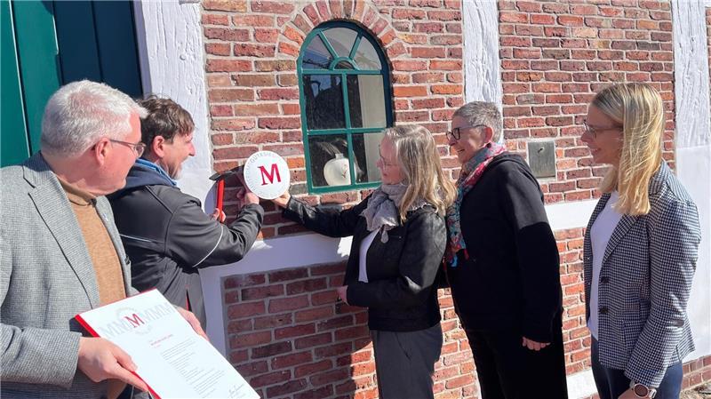 Bürgermeister Matthias Riel, Barbara Wetegrove, Dr. Kai Janofsky und Sandra Cordes schauen Hausmeister Björn Fuhrmann bei der Montage des Museumsgütesiegels zu.