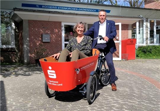 Bürgermeister Timo Gerke fährt Büchereileiterin Petra Abel im knallroten neuen Lasten-E-Bike der Samtgemeinde Lühe. Foto: Lohmann
