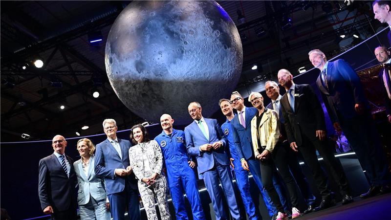 Bundeskanzler Friedrich Merz (6.v.l, CDU) steht unter anderem mit den beiden Esa-Astronauten Alexander Gerst (5.v.l) und Matthias Maurer (7.v.l) während eines Rundgangs auf der Internationalen Luft- und Raumfahrtausstellung (ILA).