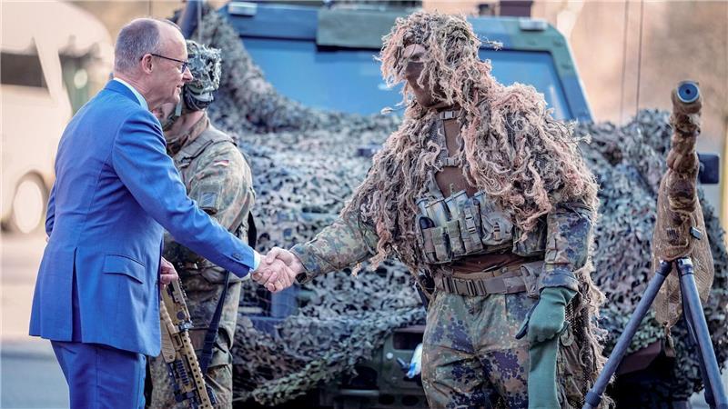 Bundeskanzler Friedrich Merz (l, CDU) wird bei der Verleihung des Fahnenbandes an das Wachbataillon in Berlin von einem Scharfschützen begrüßt.