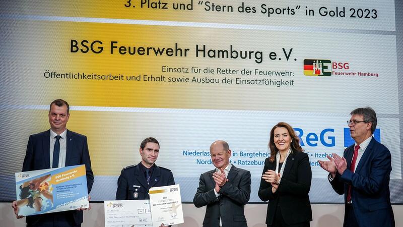 Ehrenamt: Zwei Vereine aus dem Norden ausgezeichnet Bundeskanzler Olaf Scholz (SPD, M) zeichnet zusammen mit Thomas Weikert (r), Präsident des Deutschen Olympischen Sportbundes (DOSB), und Marija Kolak (2.v.r), Präsidentin des Bundesverbandes der Deutschen Volksbanken und Raiffeisenbanken (BVR), bei der Verleihung der „Sterne des Sports“ in Gold die BSG Feuerwehr Hamburg mit dem 3. Platz aus.