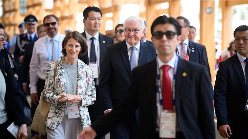 Bundespräsident Frank-Walter Steinmeier geht zusammen mit Melanie Saxinger (l), Generalkonsulin der Bundesrepublik Deutschland in Osaka-Kobe, und zahlreichen Sicherheitskräften und Personenschützern über das Gelände der EXPO 2025 Osaka.