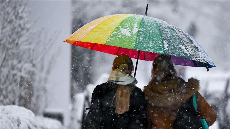Bunt und grau zugleich: Zwei Frauen gehen mit einem Schirm bei Schneefall in München.