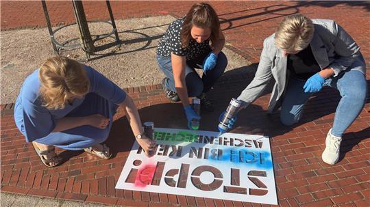 Catharina Wenzel, Mareike Wilshusen und Sabine Kiehl (von links) sprayen den ersten Schriftzug der neuen Kampagne des Landkreises Stade in Harsefeld aufs Pflaster vor einem Gully.