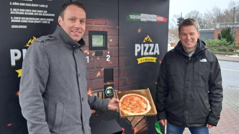 Hier gibt es Pizza aus dem Automaten – Schmeckt das? Christian Schwabe (links) und Thorsten Heitland haben einen Pizza-Automaten an der Bahnhofstraße in Stubben aufgestellt.