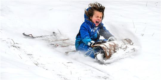 Corn Mayer, 8, fährt im Underhill Park in Spokane, Washington, mit einem Holzschlitten, der sich seit den 1960er Jahren im Besitz der Familie seiner Großmutter befindet, einen Abhang hinunter. Foto: Dan Pelle/The Spokesman-Review via AP/dpa