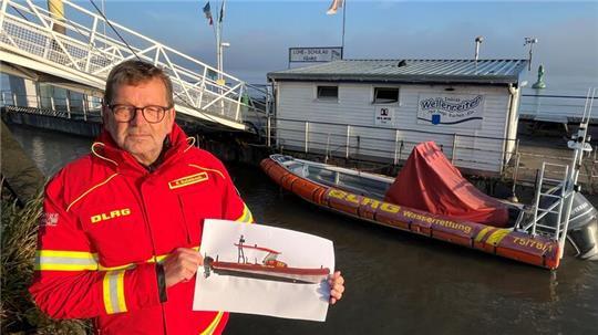 DLRG-Chef Rainer Bohmbach zeigt eine Zeichnung des neuen Motorrettungsbootes. Im Hintergrund liegt die alte Föhr Wied am Lühe-Anleger in der Elbe.
