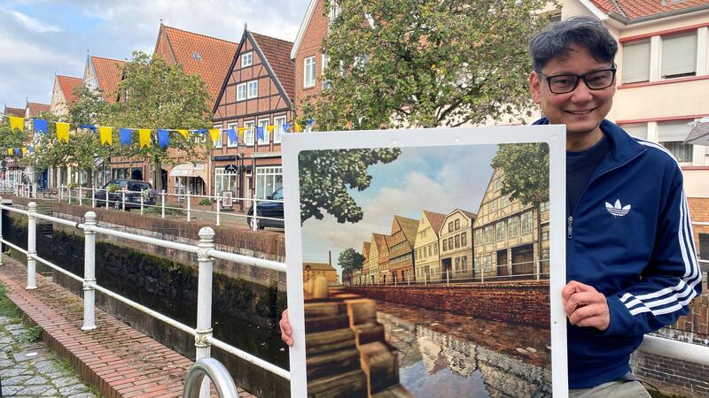 Zurück in die Vergangenheit: 6 virtuelle Zeitreisen durch Buxtehude Reiner Sprenger hält eine der alten Ansichten hoch, die als Plakate an meheren Orten am Fleth aufgehängt werden
