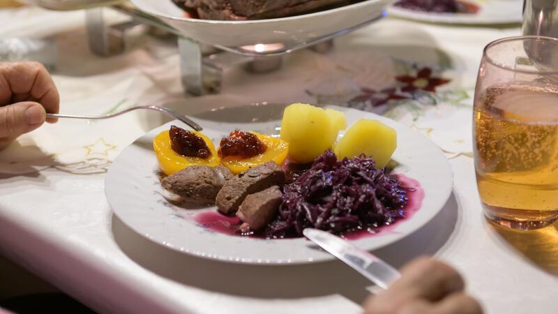 Damhirsch-Rücken mit Kartoffeln und Rotkohl sowie Preiselbeergelee auf Aprikosen liegen verzehrfertig auf einem Teller an Heiligabend.