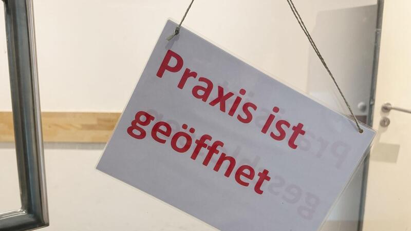 Ein Schild mit der Aufschrift „ Praxis ist geöffnet“ hängt an der Eingangstür einer Arztpraxis. (zu dpa: «Kassenärzte für Strafgebühr bei ungenutzten Arztterminen»)