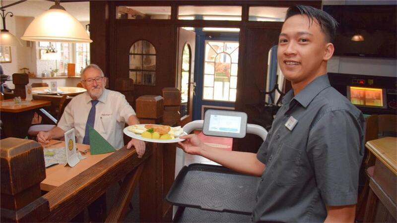 Darum geht es: Der neue Servier-Roboter soll den Mitarbeitern des Butjadinger Tors beim Decken der Tische und beim Abräumen helfen. Das Foto zeigt Gastwirt Udo Venema (links) mit Mitarbeiter Hadi Mustawan.