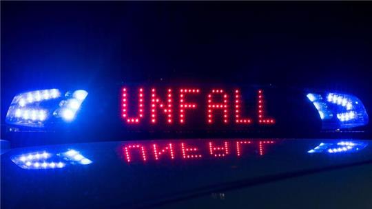 Das Blaulicht auf einem Fahrzeug der Polizei leuchtet in der Dunkelheit, während auf dem Display der Hinweis „Unfall“ zu lesen ist.